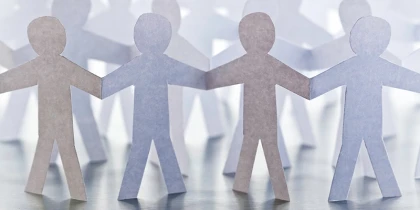 Papírové figurky stojí v řadách a drží se za ruce.